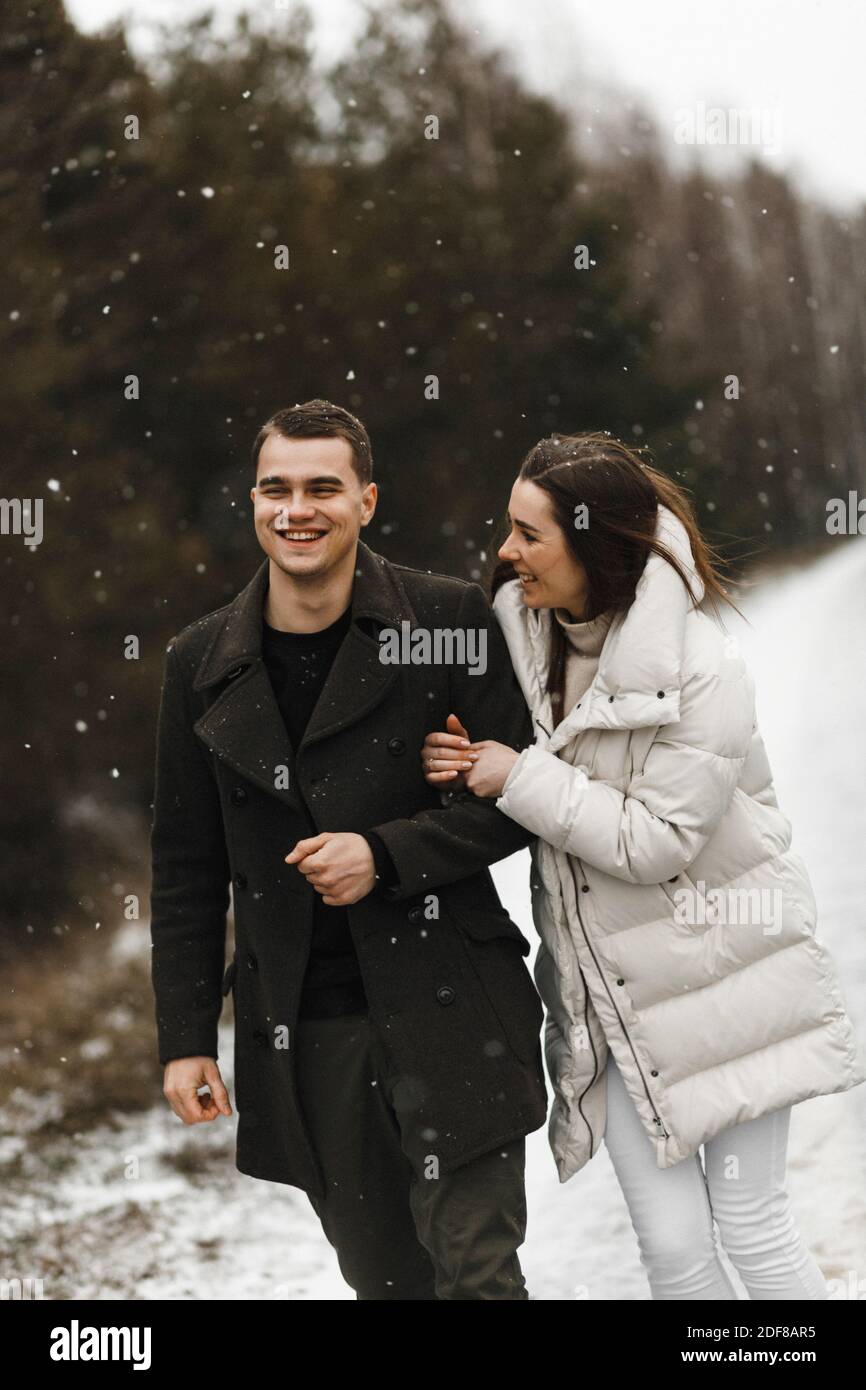 Junges lächelndes Paar, das am Hintergrund des Winterwaldes mit Kopierraum lacht. Liebe, Beziehung, Winterurlaub. Winter paar Foto-Ideen Stockfoto