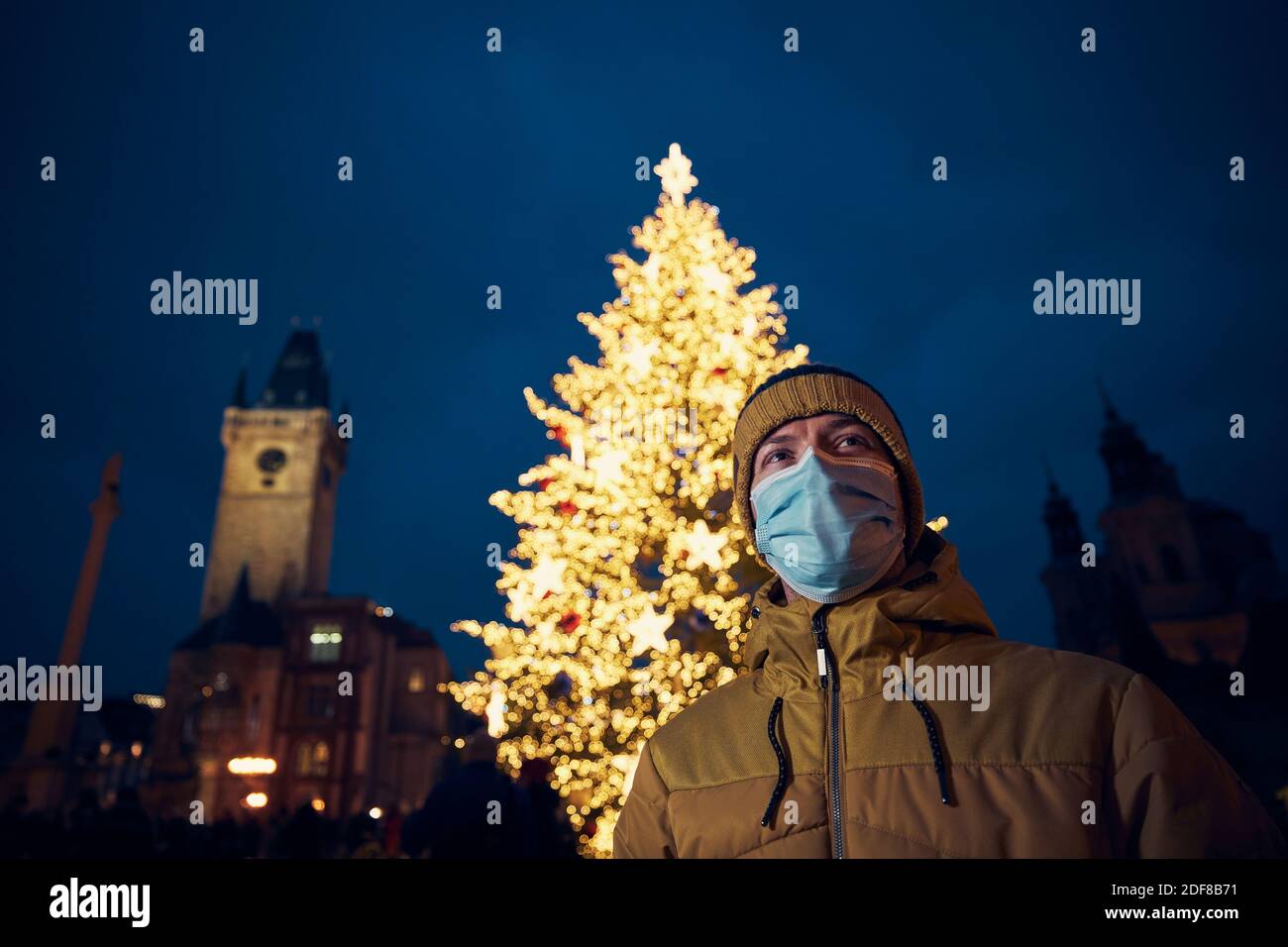 Junger Mann mit Gesichtsmaske gegen Weihnachtsbaum in Prag. Themen Coronavirus-Pandemie während der Weihnachtsfeiertage und persönliche Verantwortung. Stockfoto