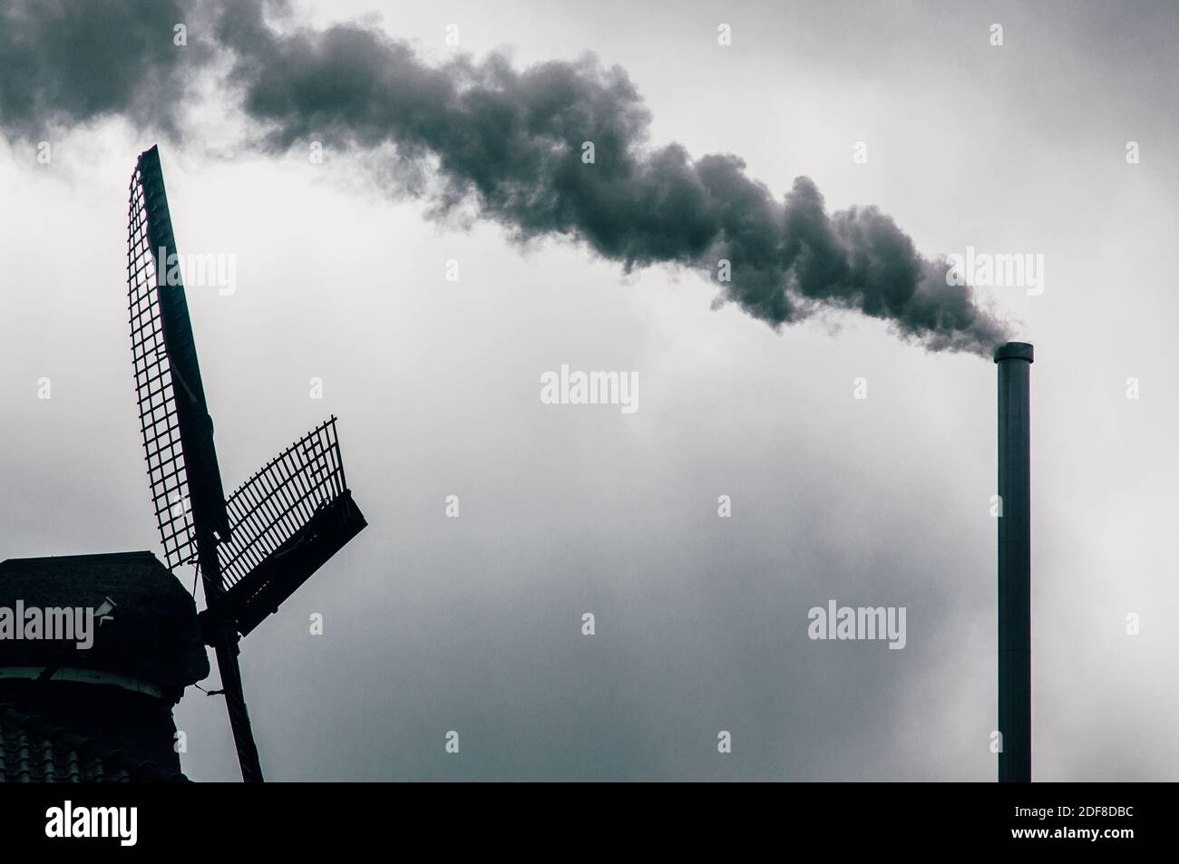Windmühle und Industriekamin an einem dunklen und bewölkten Tag In Zaanse Schans in den Niederlanden mit Verschmutzung und C02 Stockfoto