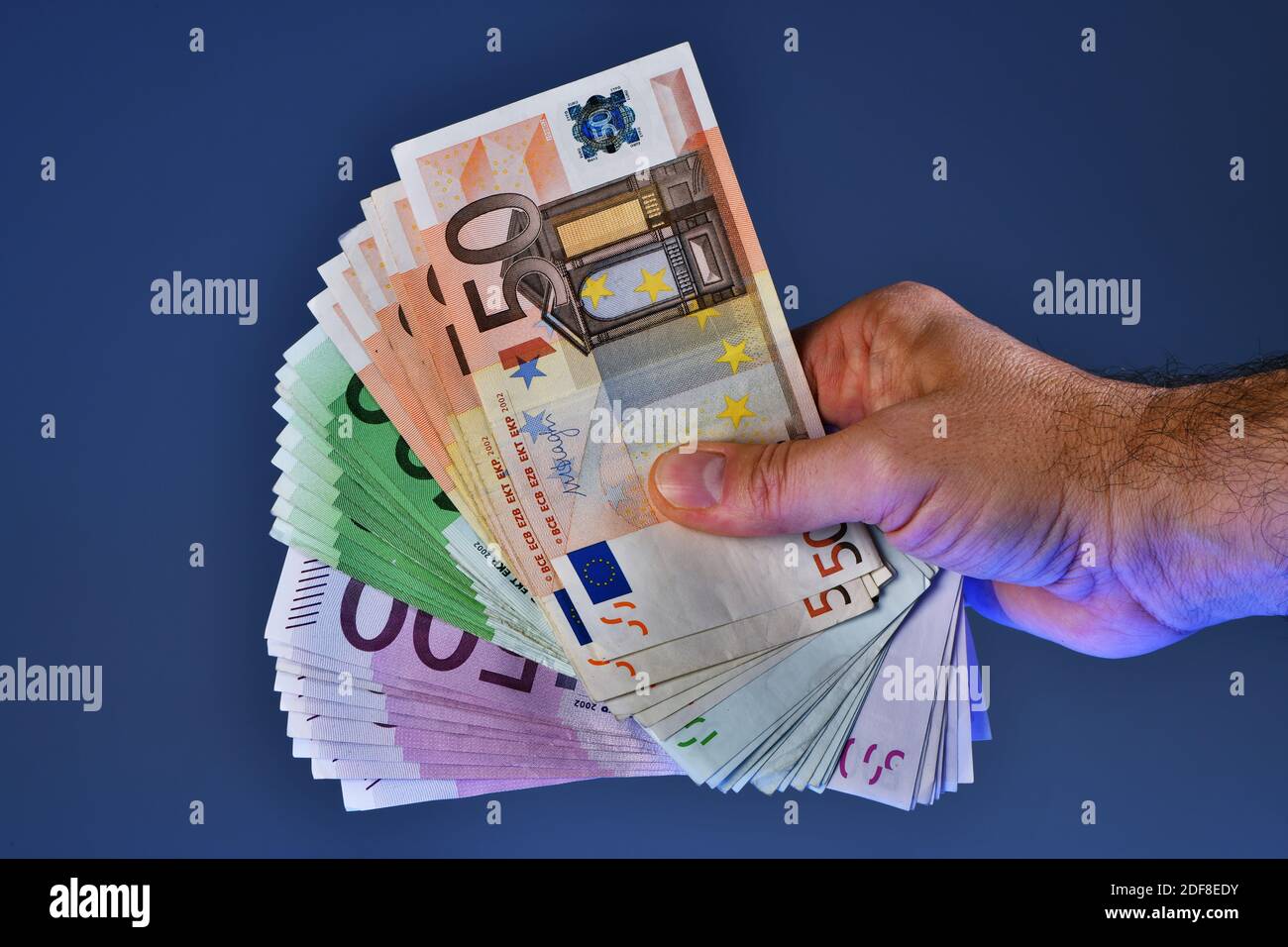 Eine Mann Hand zeigt 20,000 Euro in 100 Euro und 500 Euro Banknoten auf blauem Hintergrund. Kaufen Sie ein neues Auto Stockfoto