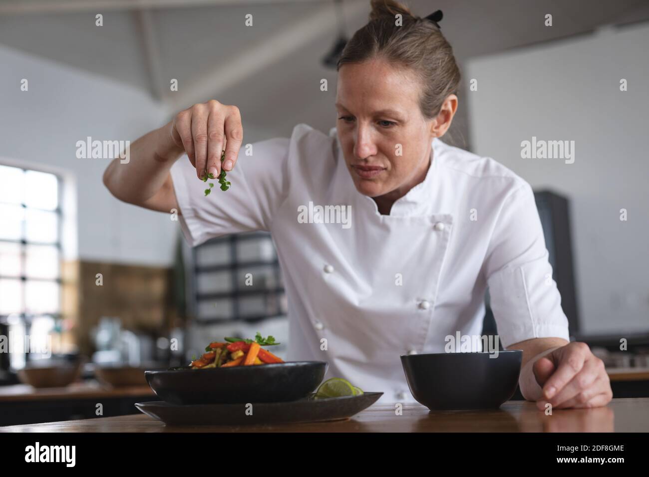 Ältere weibliche kaukasische Köchin garniert Salatgericht in der Restaurantküche Stockfoto