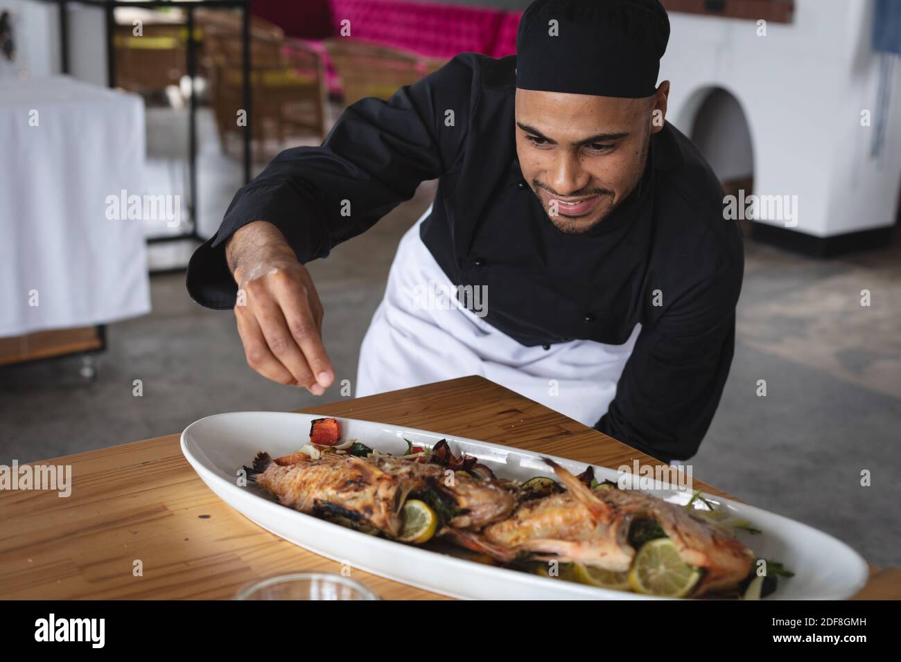 Männlicher Koch aus dem Nahen Osten, der gerösteten Fischgerichten Salz zuführt In der Speiseteller in der Restaurantküche Stockfoto