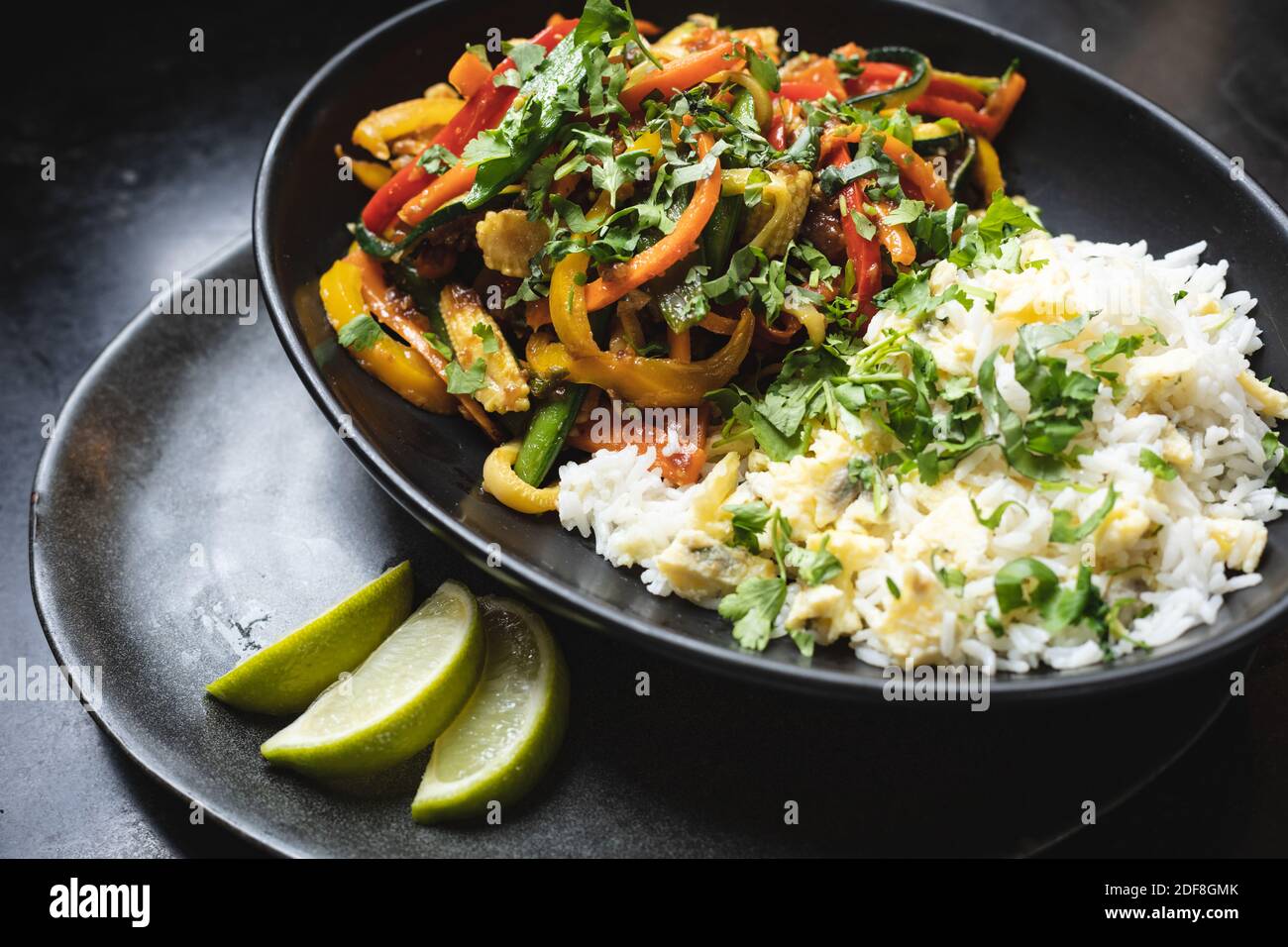 Nahaufnahme der Schüssel mit Reis und Salatgericht Mit frisch geschnittenen Limetten auf schwarzer Oberfläche Stockfoto