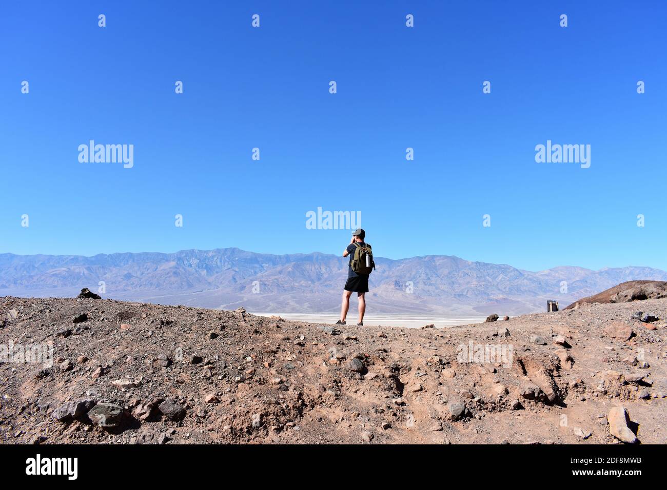 Ein männlicher Wanderer mit Rucksack steht auf einem kleinen Hügel am Trail Kopf zum Natural Bridge Canyon mit Blick auf Badwater Basin und Death Valley, USA Stockfoto