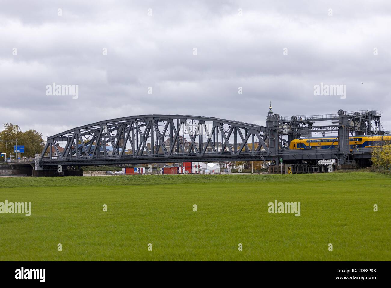 Landschaft mit Stahlbau Bahngleise Brücke über den Fluss IJssel Mit einer holländischen Eisenbahn, die über sie fährt Bewölktes Wetter Stockfoto