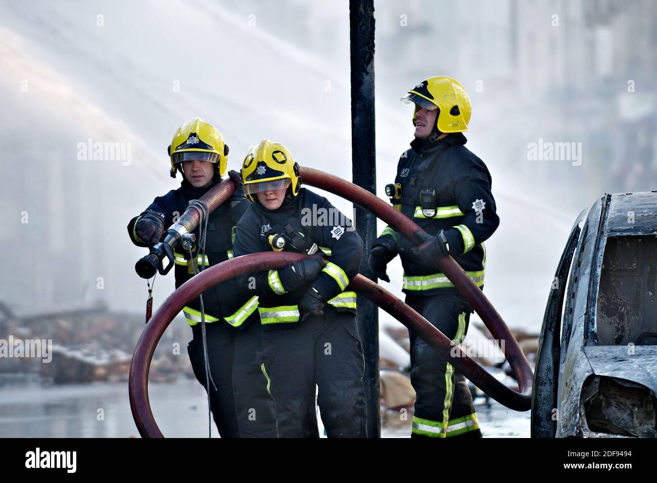 London, England - 9. August 2011: Feuerwehrleute in London nach den Unruhen in Croydon ziehen einen Schlauch auf eine neue Position drei Feuerwehrleute dra Stockfoto