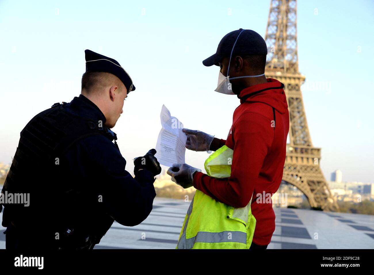 Französische Polizeibeamte prüfen die Dokumente eines Mannes vor dem Eiffelturm in Paris, Da in Frankreich eine strikte Sperre in Kraft tritt, um die Ausbreitung von COVID-19 zu stoppen. Nach der Ankündigung des französischen Präsidenten Emmanuel Macron über die strikten Regeln für die Heimbindung der Franzosen aufgrund eines Ausbruchs der Coronavirus-Pandemie (COVID-19) am 18. März 2020 in Paris, Frankreich. Die Franzosen werden zu Hause bleiben müssen, Frankreich hat alle Schulen, Theater, Kinos und eine Reihe von Geschäften geschlossen, wobei nur diejenigen, die Lebensmittel und andere wichtige Dinge verkaufen, offen bleiben dürfen. Unter Strafe von Sanktionen, verbieten Stockfoto
