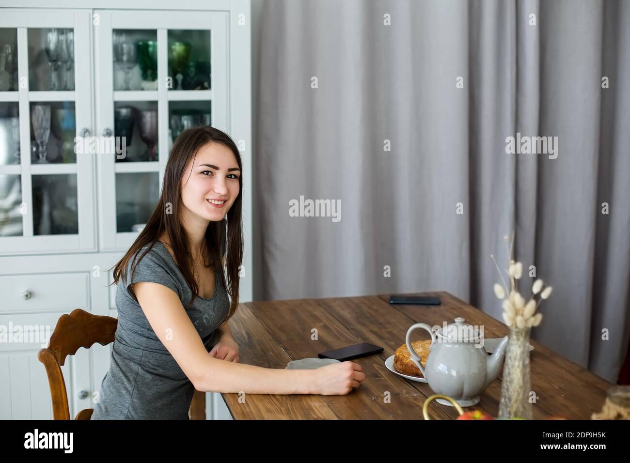 Brunette Mädchen sitzt in der Küche an einem Holztisch, ein Wasserkocher mit Tee Stockfoto