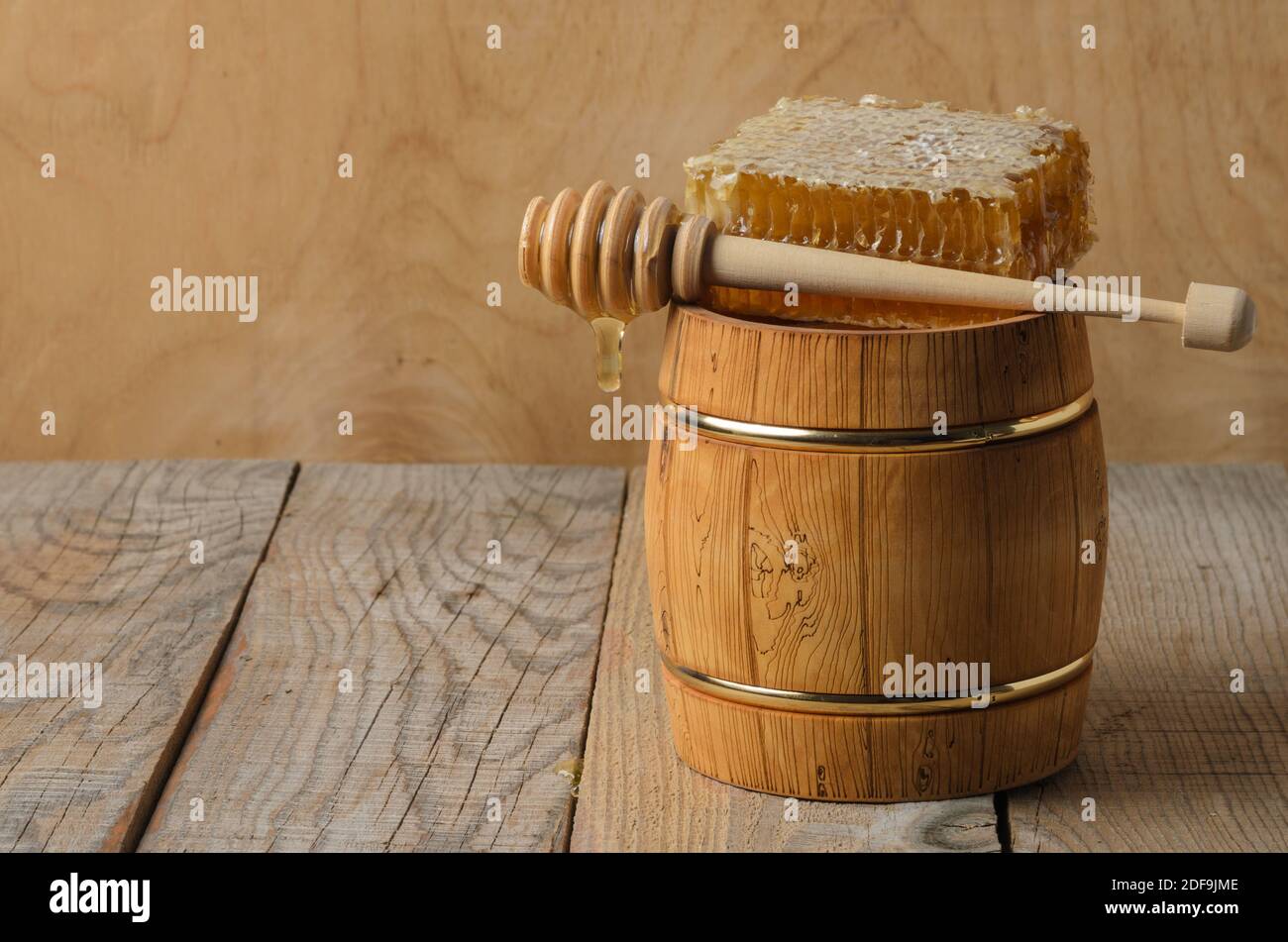 Holzfass mit Honig, Honig in einer Wabe mit einem Holzlöffel und Tropfen auf den Tisch. Selektiver Fokus. Stockfoto
