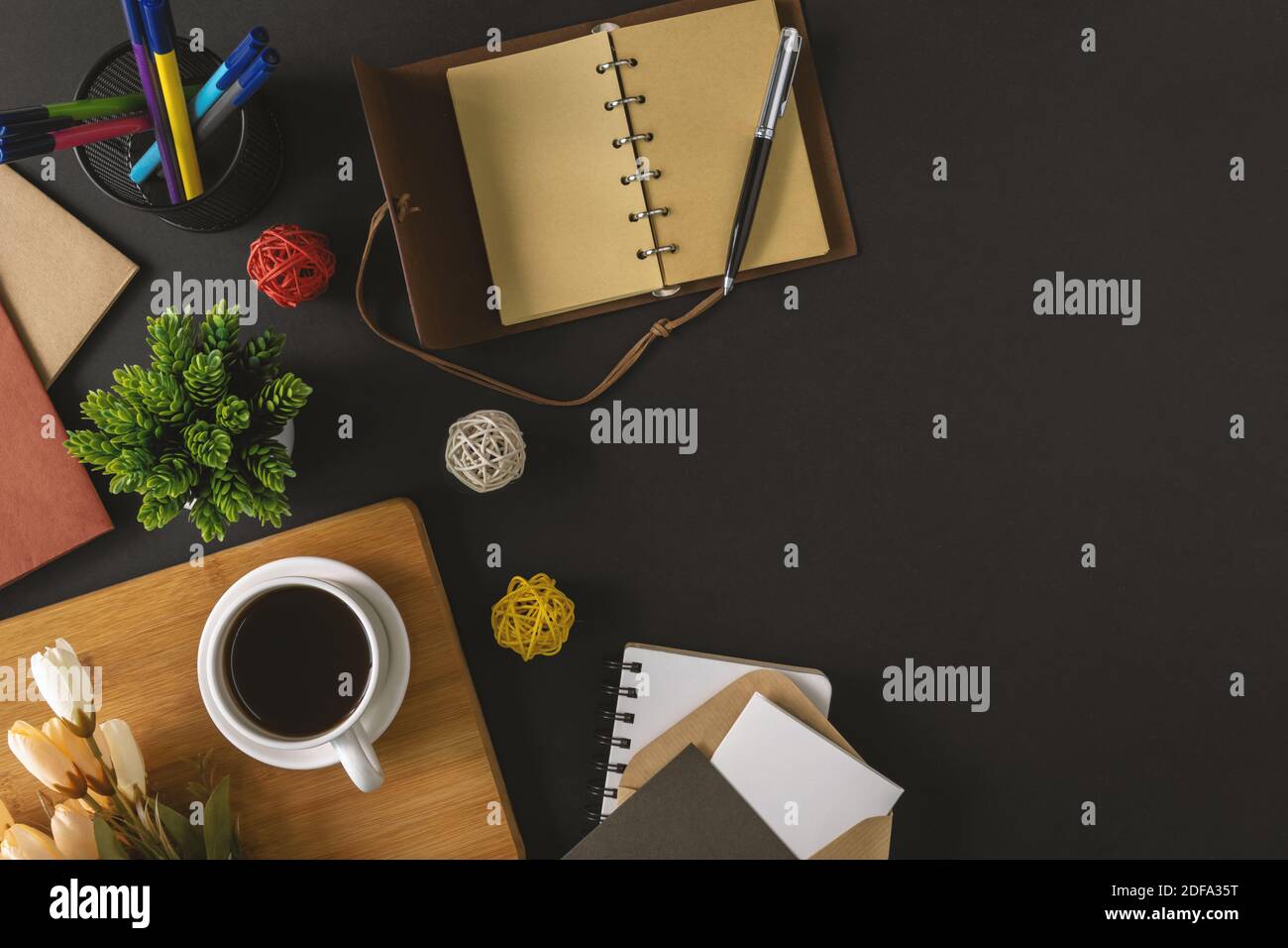 Rustikaler Notizblock, Stift und Kaffee auf schwarzem Hintergrund. Kühl und ruhig Bürotisch Stillleben. Stockfoto
