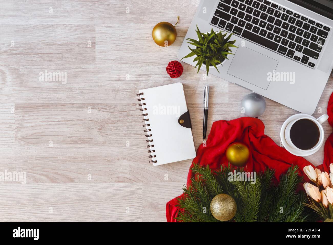 Laptop und Notizblock mit Ornamentkugeln auf Holztisch. Bürotisch an Weihnachten. Stockfoto