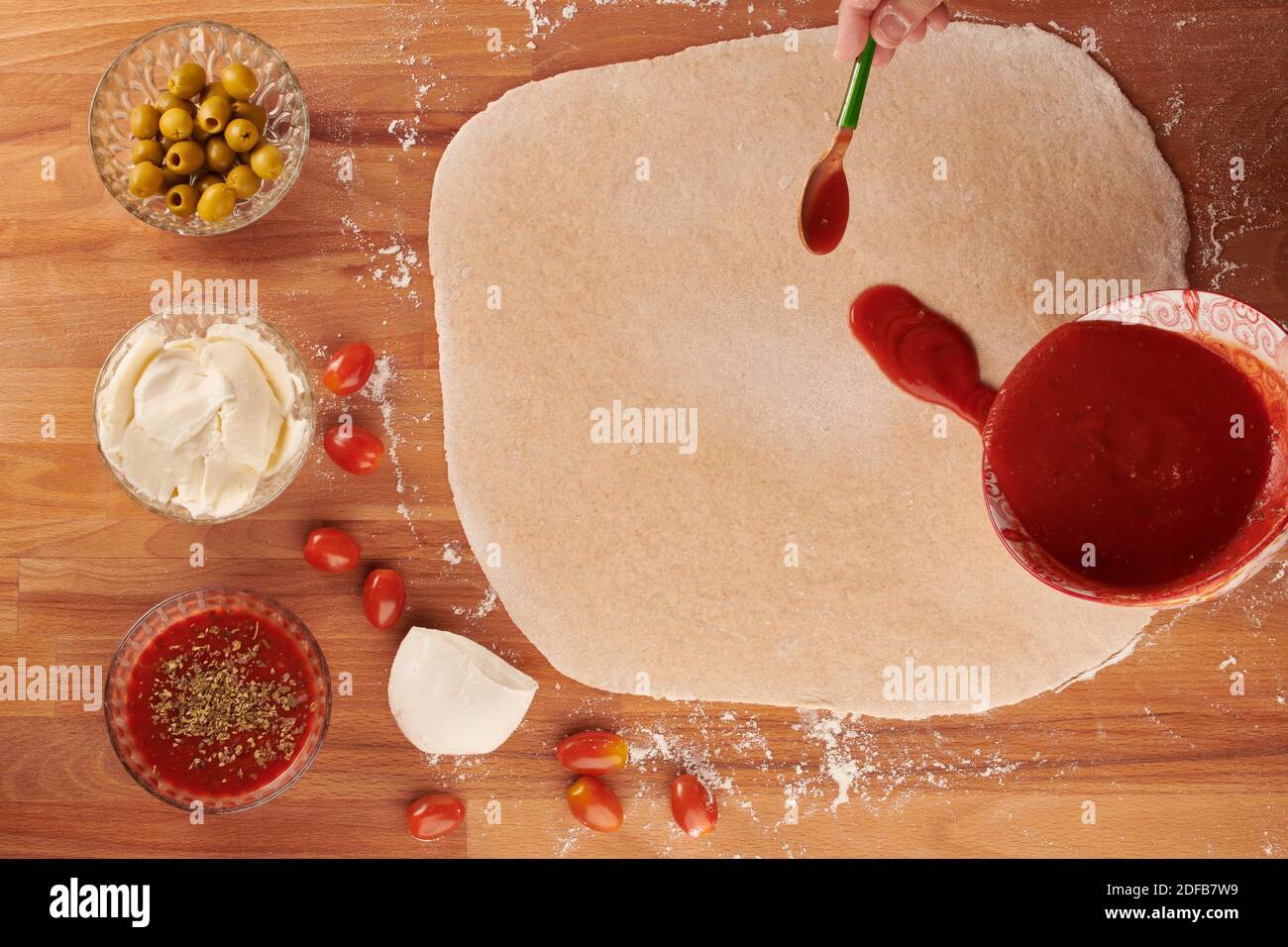 Italienische Pizza Schritt für Schritt mit Zutaten für handgemachte Pizza: Hinzufügen von Tomatensauce Stockfoto