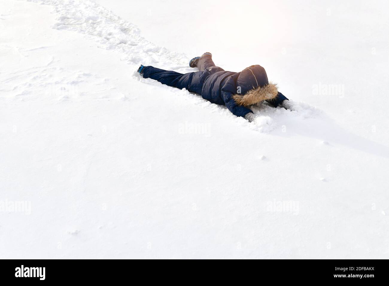 Ein Kind in einem Winterjumpsuit liegt in voller Höhe im Schnee ausgebreitet, mit dem Gesicht nach unten, mit ausgestreckten Armen nach vorne. Stockfoto
