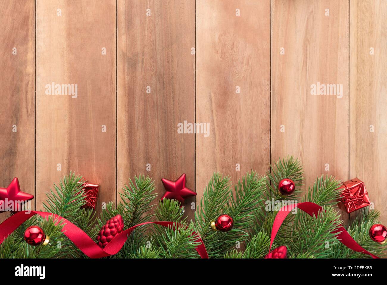 Grüne Weihnachtsbaumblätter mit leuchtend roten Ornamenten auf Holzhintergrund, Bordüre Stockfoto