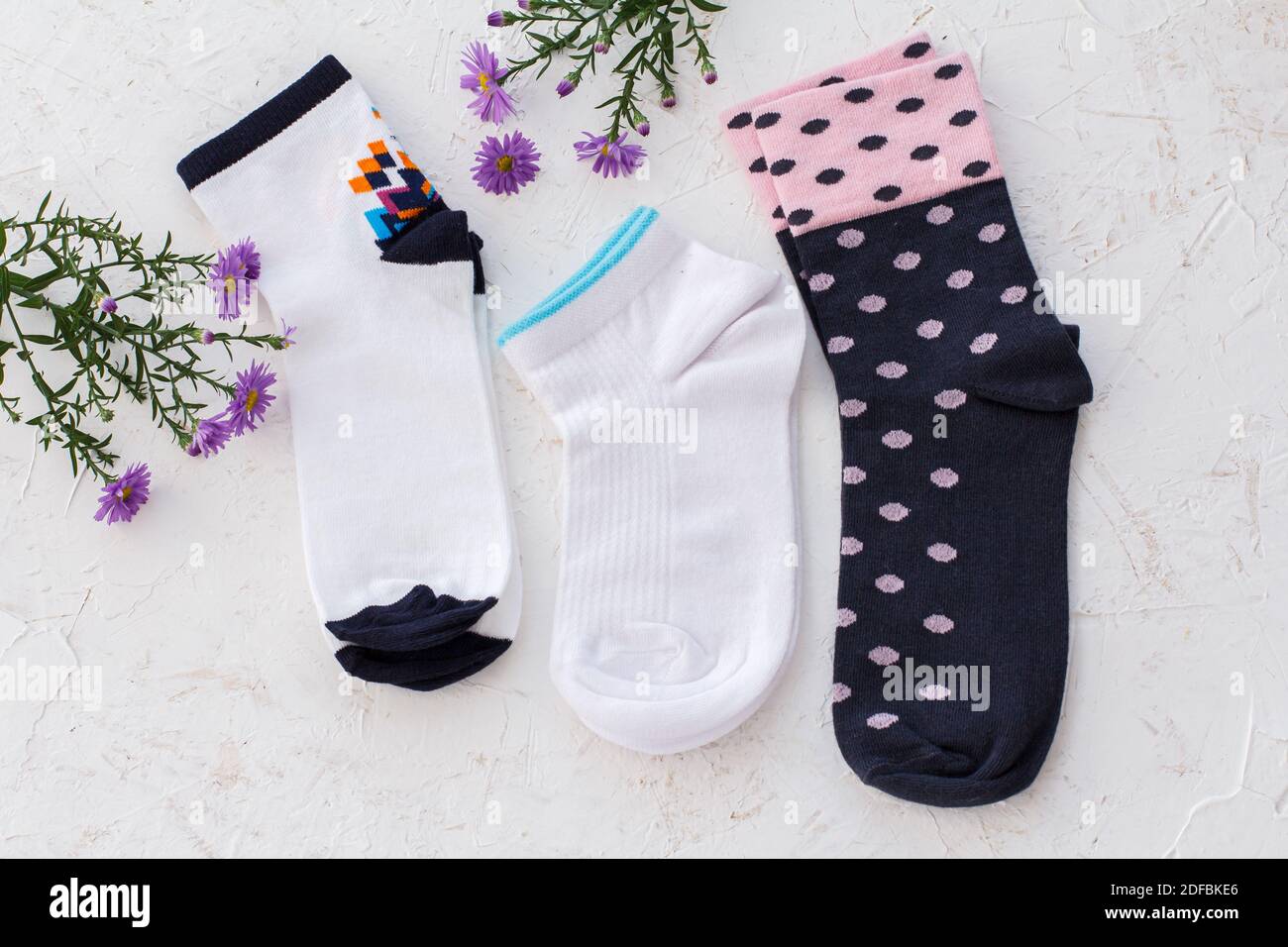 Drei Paar Damensocken und Blumen auf weißem strukturiertem Hintergrund, Draufsicht. Stockfoto