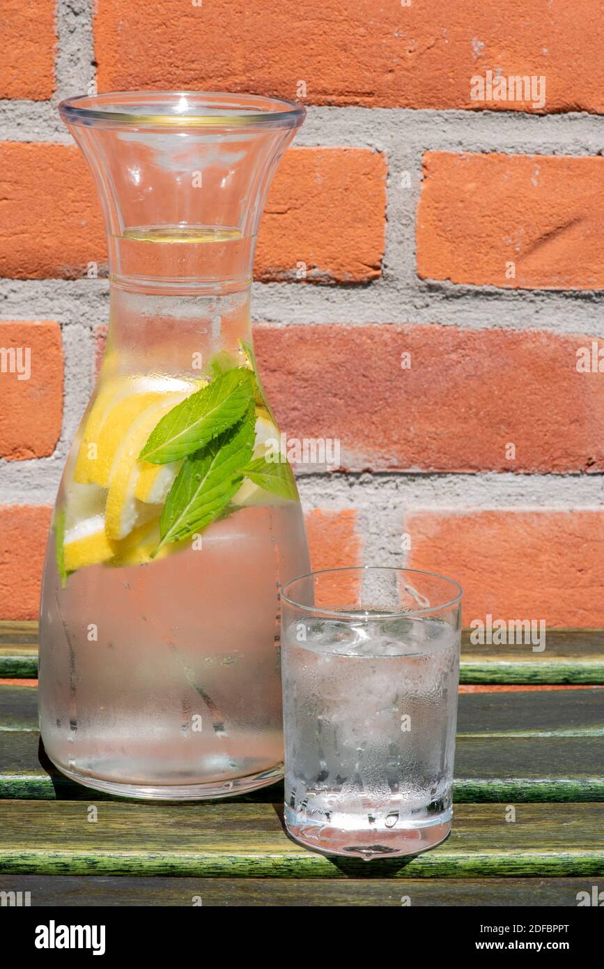 Sommer Karaffe und Glas kaltes Wasser auf Holz Tisch mit Backsteinmauer von zu Hause im Hintergrund Stockfoto