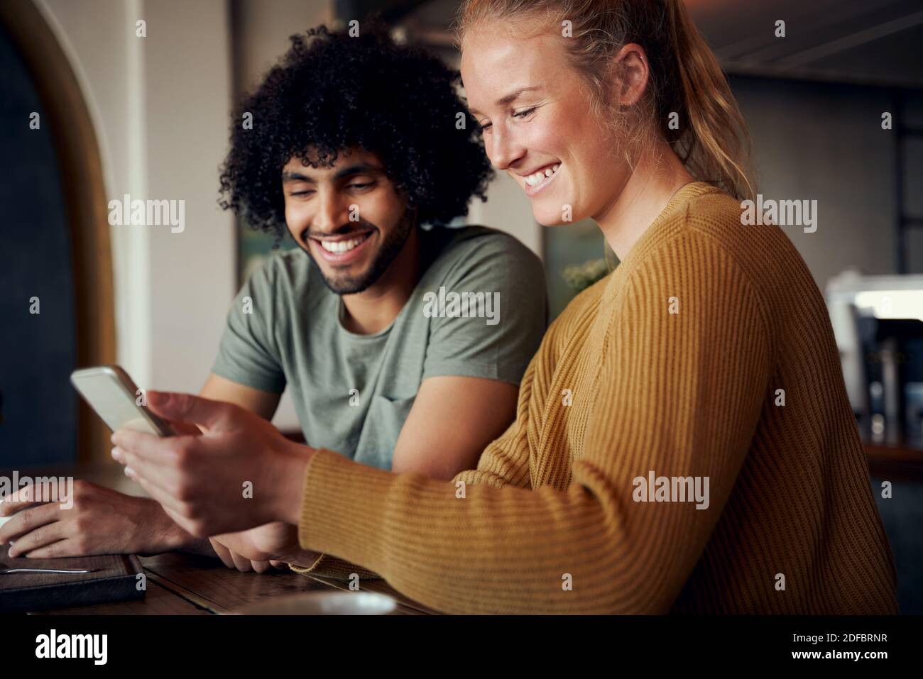 Schöne Frau und schöner Mann beim Video in Smartphone und Lachend im Café Stockfoto