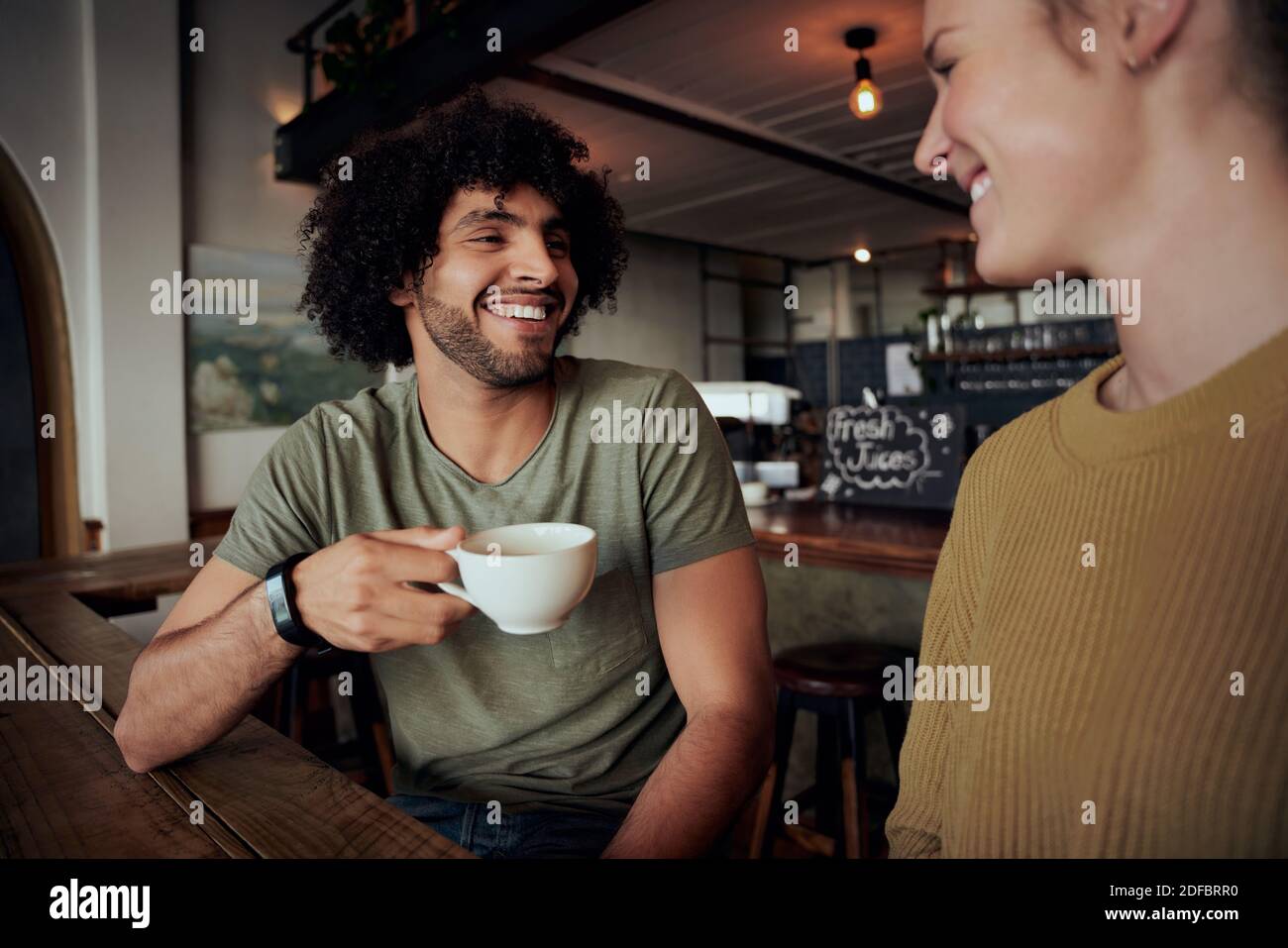 Schöner junger Mann mit lockigen Haaren hält Kaffeetasse sitzen Mit schöner Frau und im Café reden Stockfoto