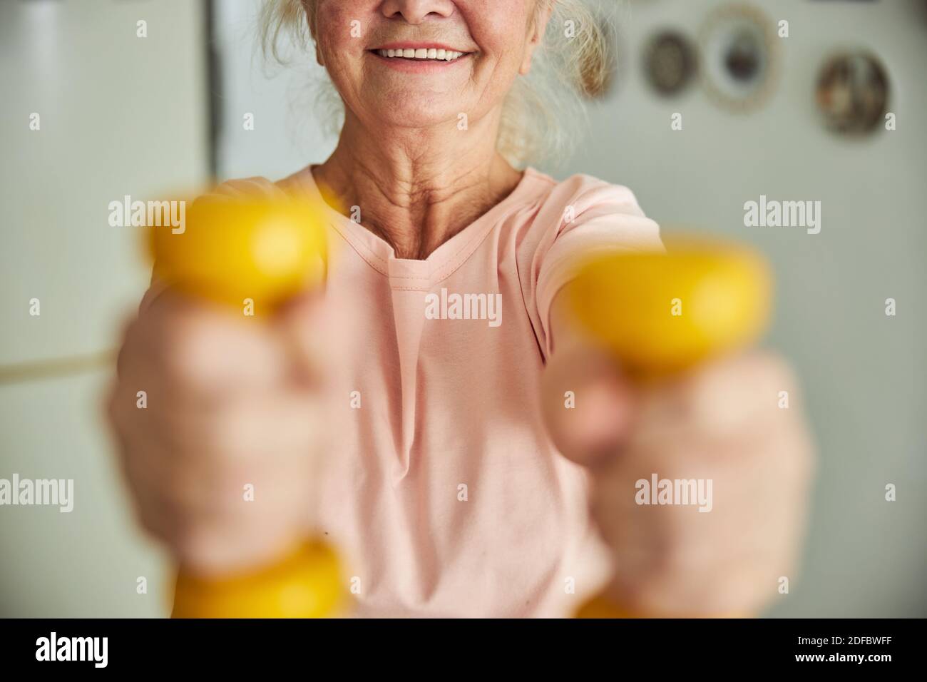 Fröhliche ältere Frau macht Übung mit Hanteln zu Hause Stockfoto