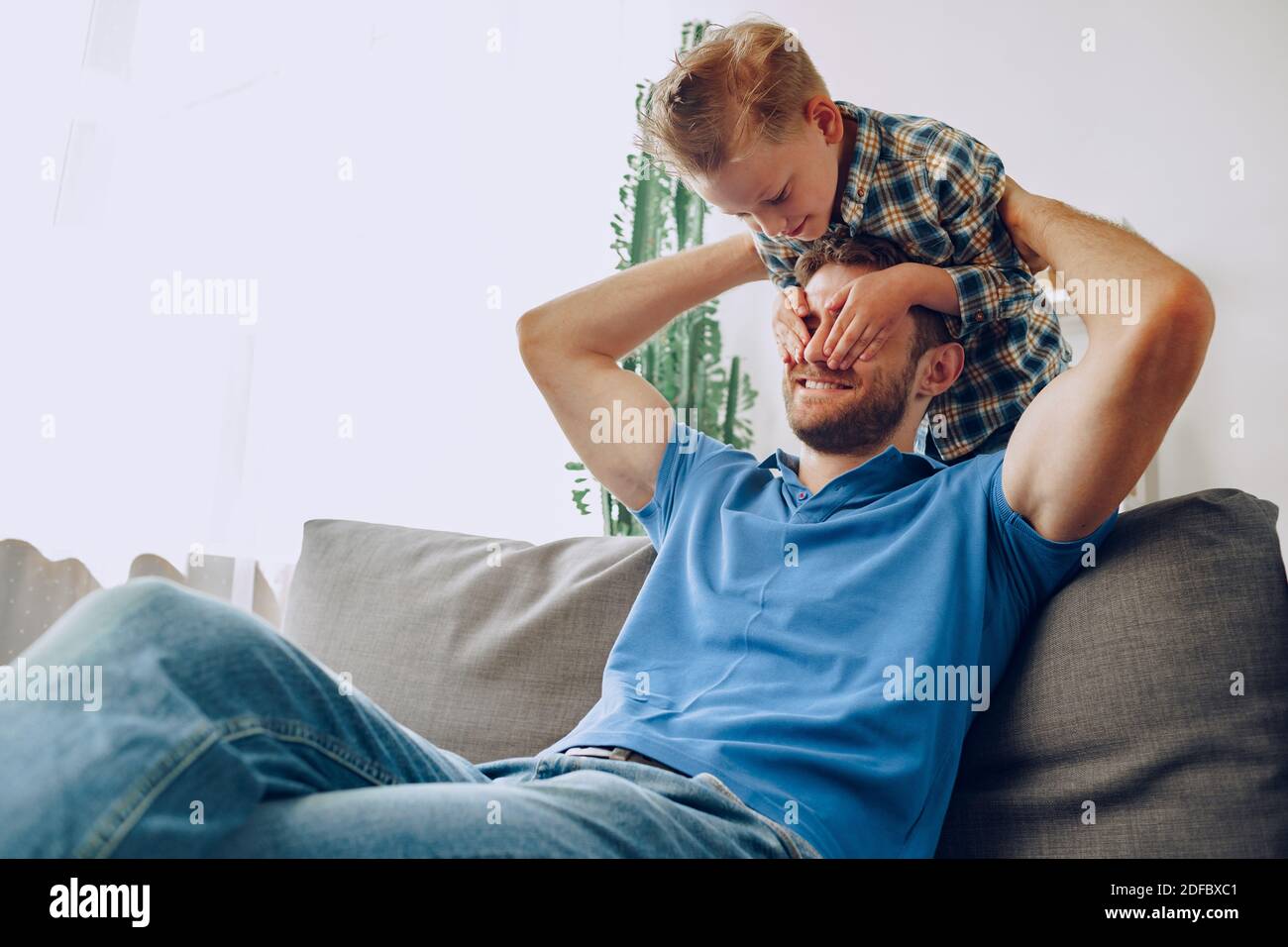 Der kleine Junge bedeckt die Augen des Vaters mit den Händen im Leben Zimmer Stockfoto