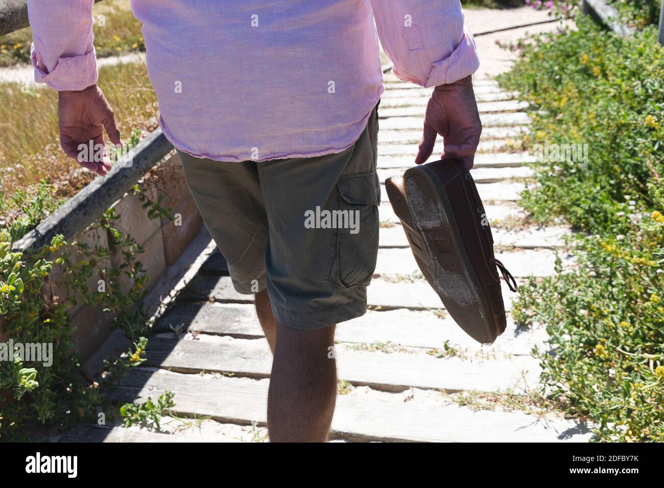 Mittelteil des älteren Kaukasiers, der Schuhe hält und die Stufen hinunter läuft Strand Stockfoto