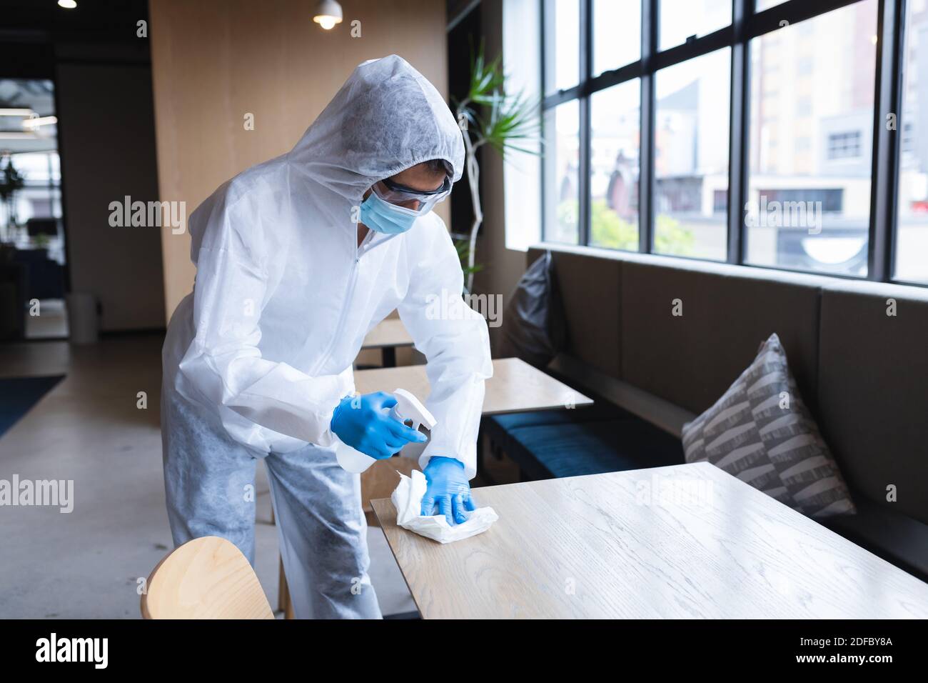 Gesundheitsarbeiter in Schutzkleidung sprühen Desinfektionsmittel auf Tisch Stockfoto