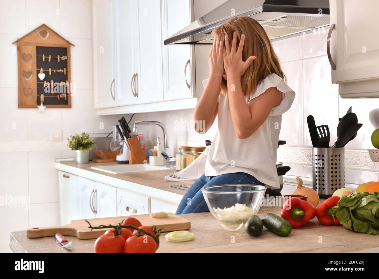 Kleines Mädchen auf Küchenbank sitzen und Essen mit Händen zubereiten Auf dem Gesicht zu Hause Stockfoto
