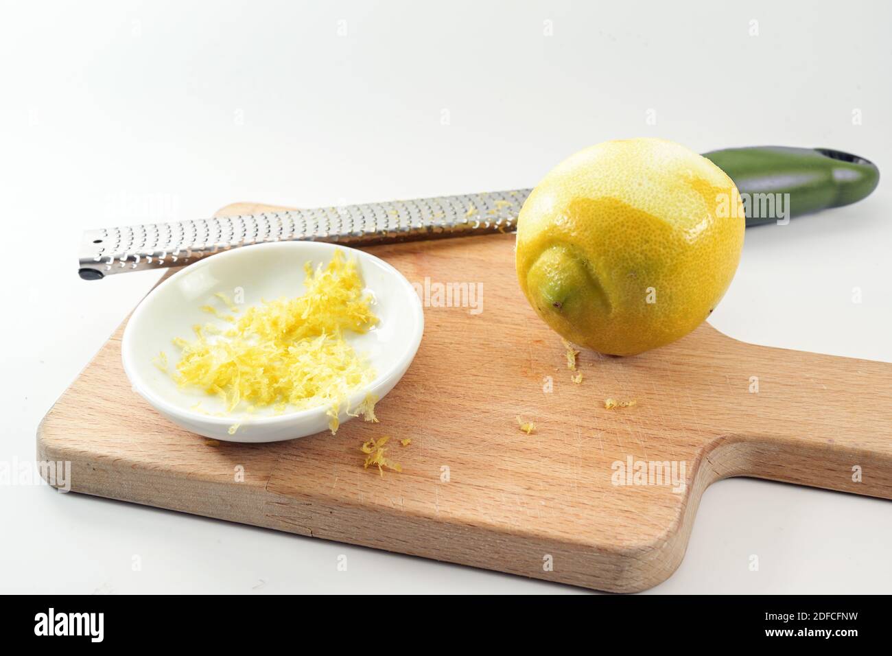 Geriebene Zitronenschale in einer kleinen Schüssel, Obst und Reibe auf einem hölzernen Küchentafel, heller Hintergrund, Kopierraum, ausgewählter Fokus, enge Schärfentiefe Stockfoto