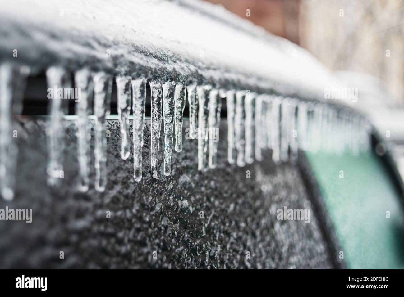 Auto mit Eis und Eiszapfen nach Glatteisregen bedeckt. Eisbedecktes Autofenster aus der Nähe. Schlechtes Winterwetter, Eissturm. Stockfoto