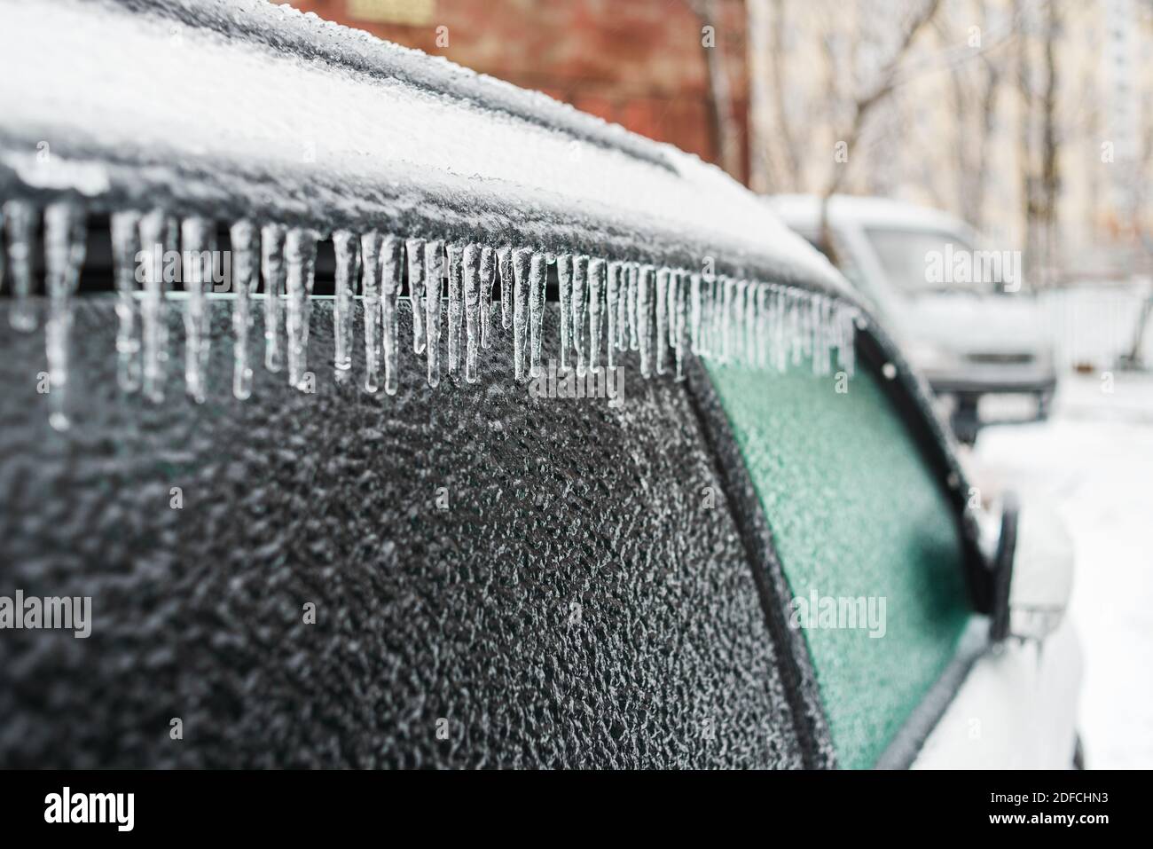 Eisbedecktes Autofenster aus der Nähe. Weißes Auto bedeckt mit Eis und Eiszapfen nach eisigen Regen. Schlechtes Winterwetter, Eissturm. Stockfoto