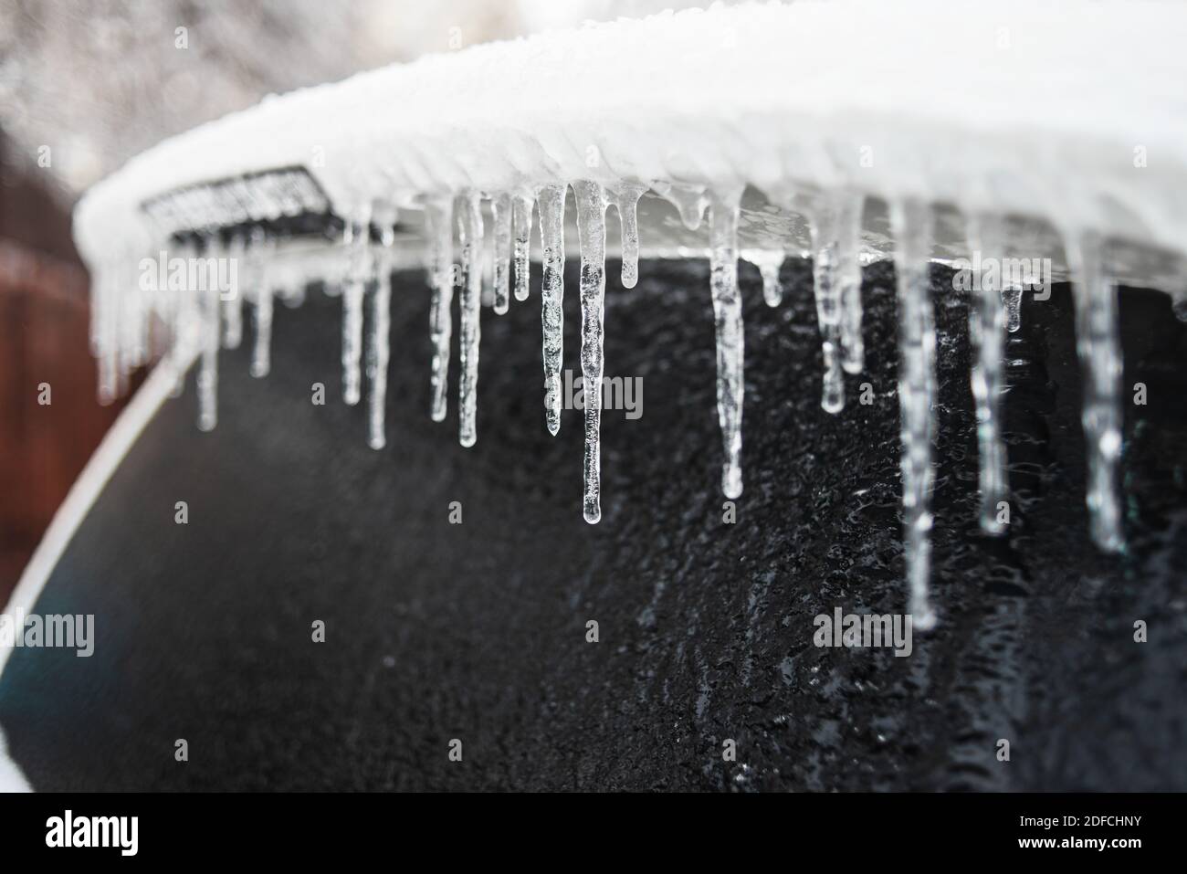 Eisbedecktes Autofenster aus der Nähe. Auto mit Eis und Eiszapfen nach Glatteisregen bedeckt. Schlechtes Winterwetter, Eissturm. Stockfoto