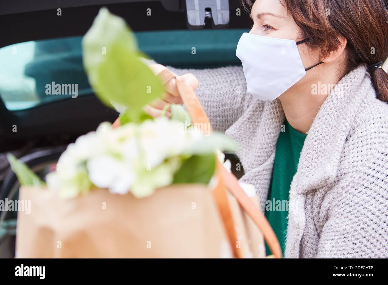 Frau mit OP-Maske trägt Tasche mit Blumen in den Händen Aus dem Kofferraum Stockfoto