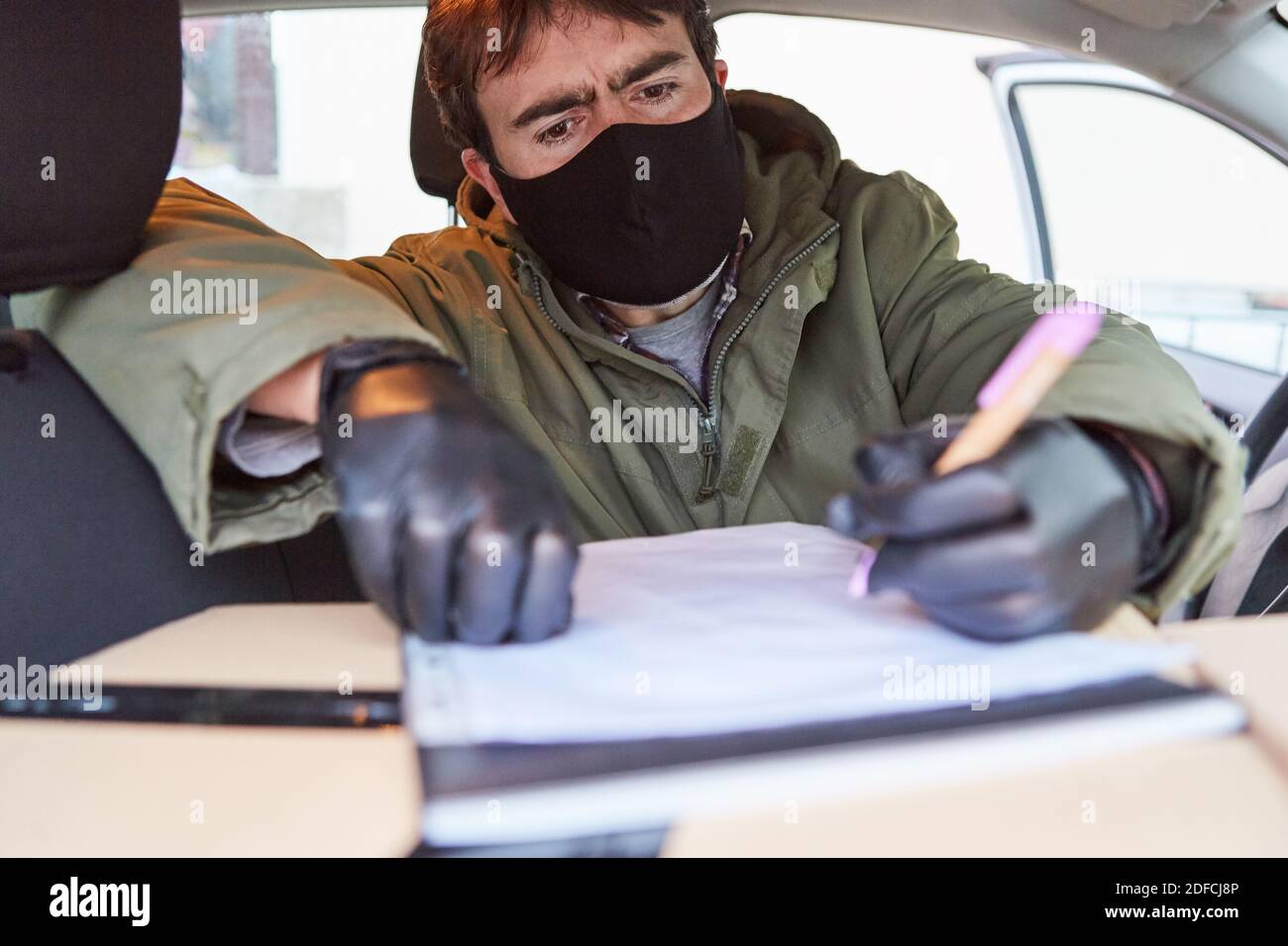 Lieferservice Paketzustellung Mann mit Gesichtsmaske prüft Lieferung Im Innenraum seines Fahrzeugs Stockfoto