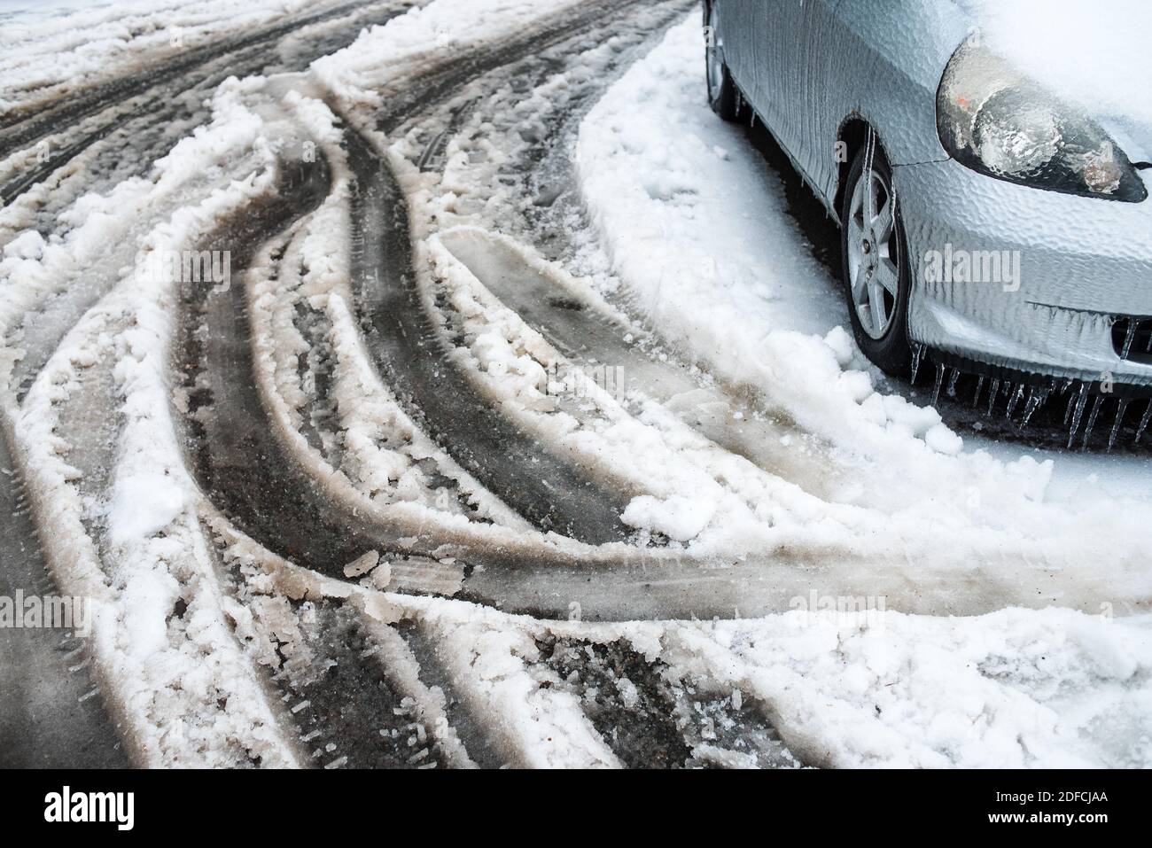 Spuren von den Rädern von Autos auf einer nassen verschneiten Straße. Auto bedeckt mit Eis, Schnee und Eiszapfen. Stadt im Winter. Eissturmwetter. Stockfoto