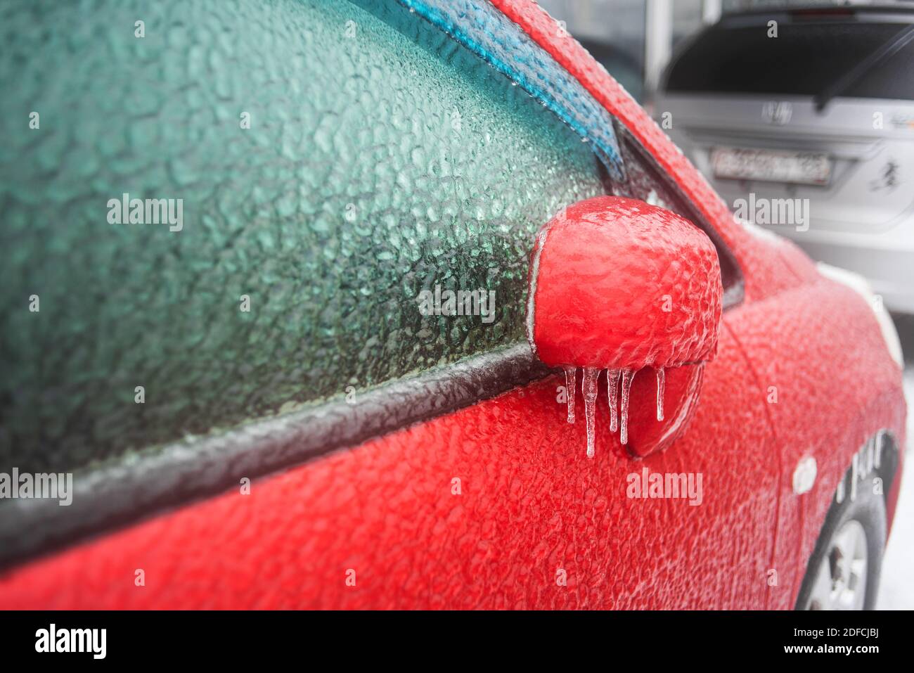 Eisbedecktes Autofenster aus der Nähe. Rotes Auto bedeckt mit Eis und Eiszapfen nach eisigen Regen. Schlechtes Winterwetter, Eissturm. Stockfoto