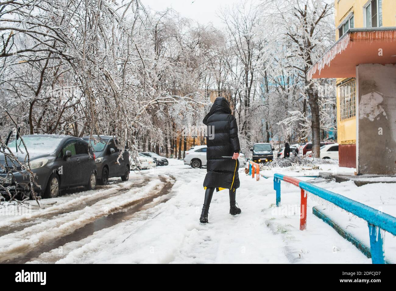 Blick auf die Stadt und die Straßen bei schlechtem Schneewetter. Frau geht auf einer rutschigen Straße die Straße hinunter. Eissturmzyklon. Stadt im Winter. Stockfoto