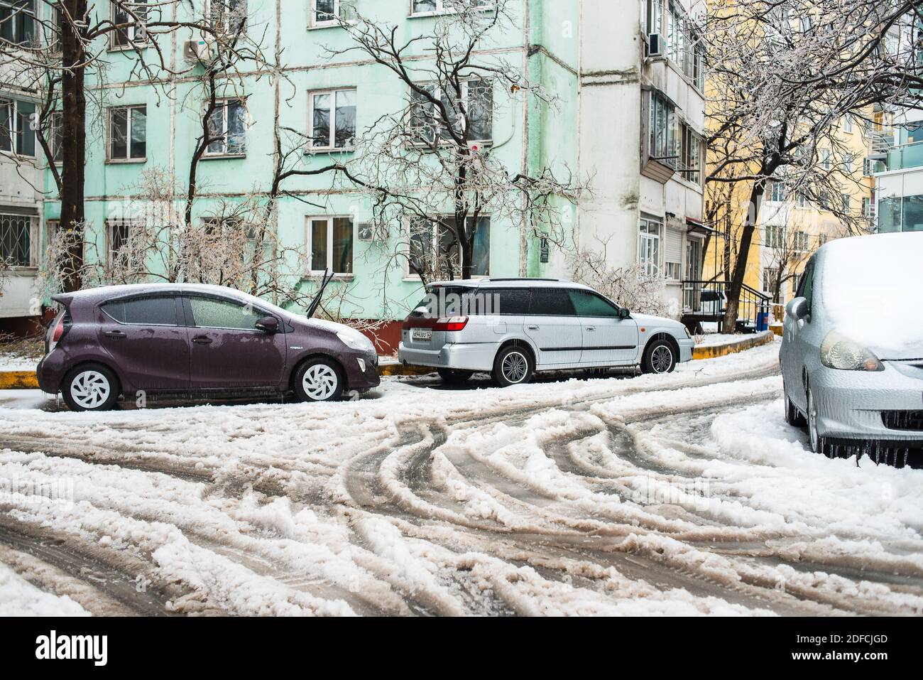 Spuren von den Rädern von Autos auf einer nassen verschneiten Straße. Auto bedeckt mit Eis, Schnee und Eiszapfen. Eissturmzyklon. Frostige Szenen im Winter. Stockfoto