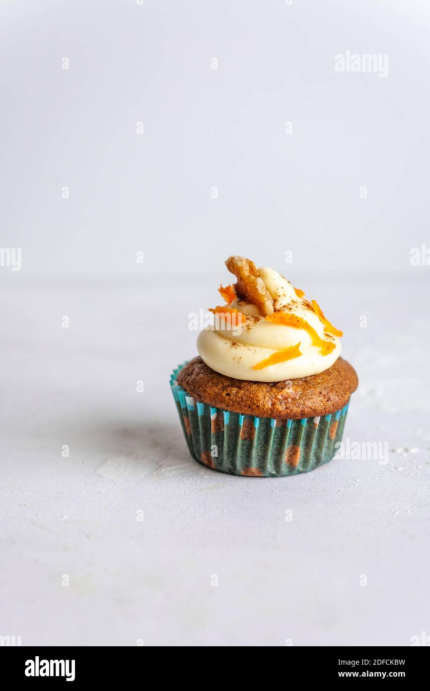 Eine einzelne Muffins in einem blauen Halter mit Glasur und Karottenrasur auf weißem Hintergrund, vertikal Stockfoto