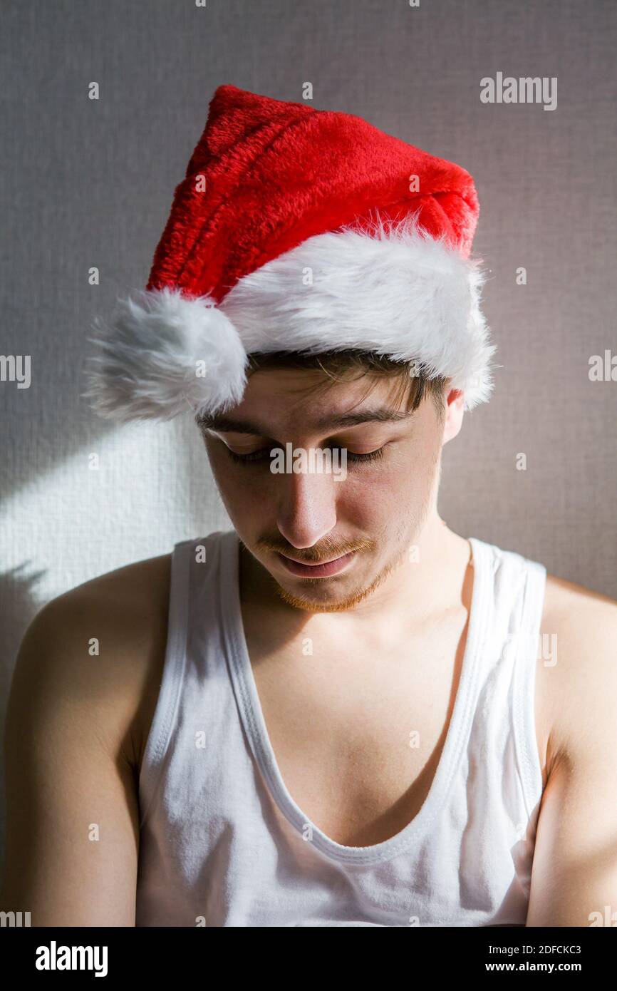 Trauriger junger Mann in Santa hat an der Wand in Das Zimmer Stockfoto
