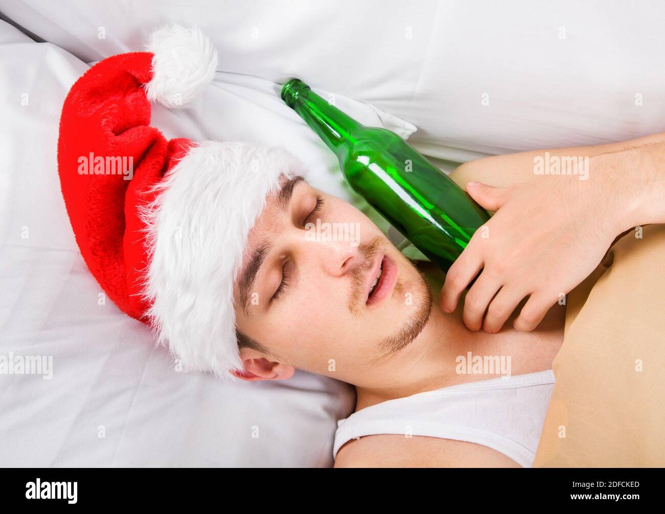 Mann in Santa hat schlafen im Bett mit einem Bier Stockfoto