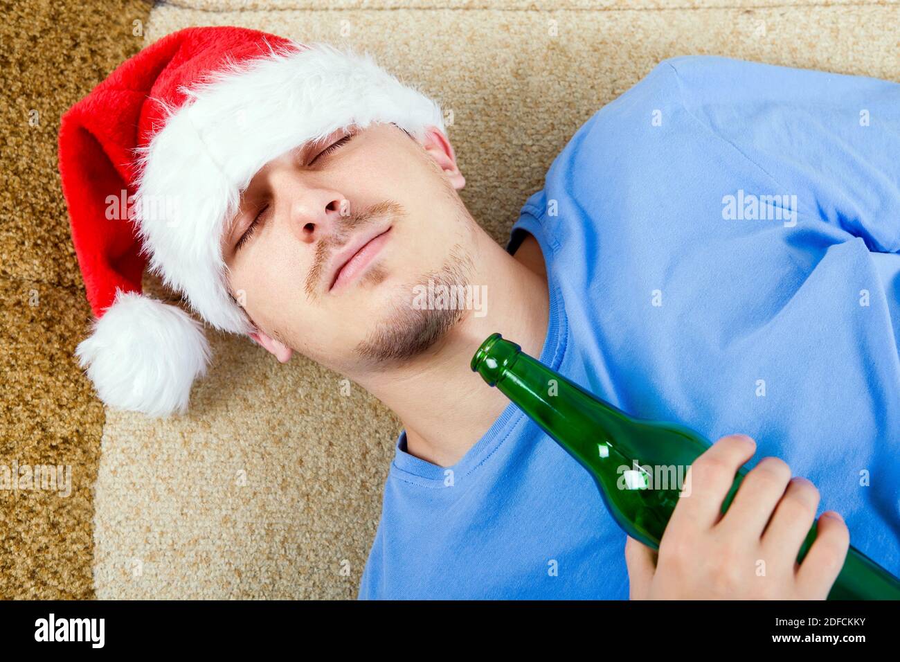 Ein Mann in Santa hat schlafen auf dem Sofa mit Ein Bier Stockfoto