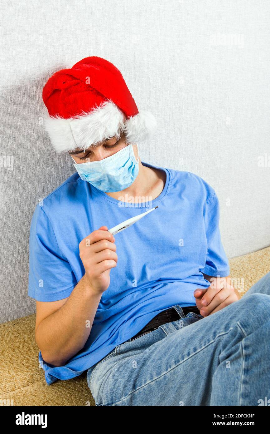 Kranker junger Mann in Weihnachtsmütze und der Grippe Maske Mit einem Thermometer Stockfoto