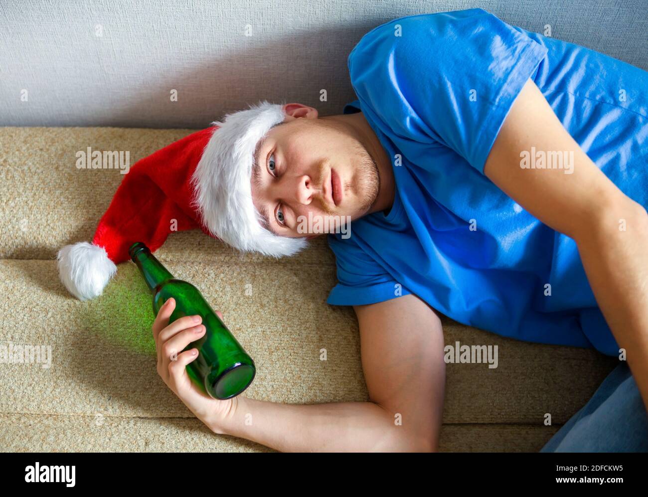 Junger Mann im Weihnachtsmütze auf dem Sofa mit einem Bier Stockfoto