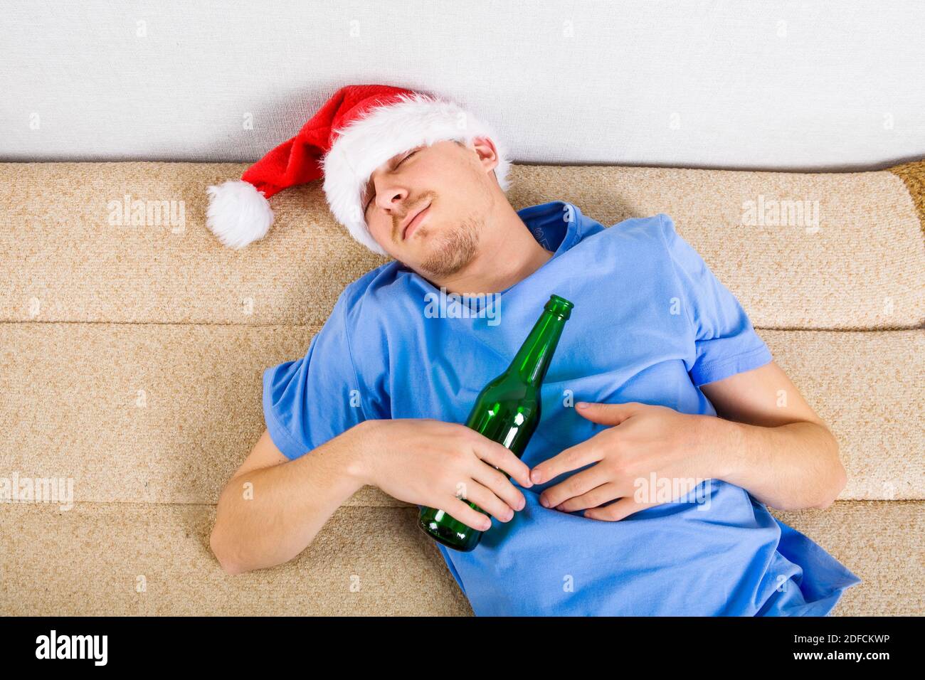 Junger Mann in Santa hat schlafen auf dem Sofa mit Eine Bierflasche Stockfoto