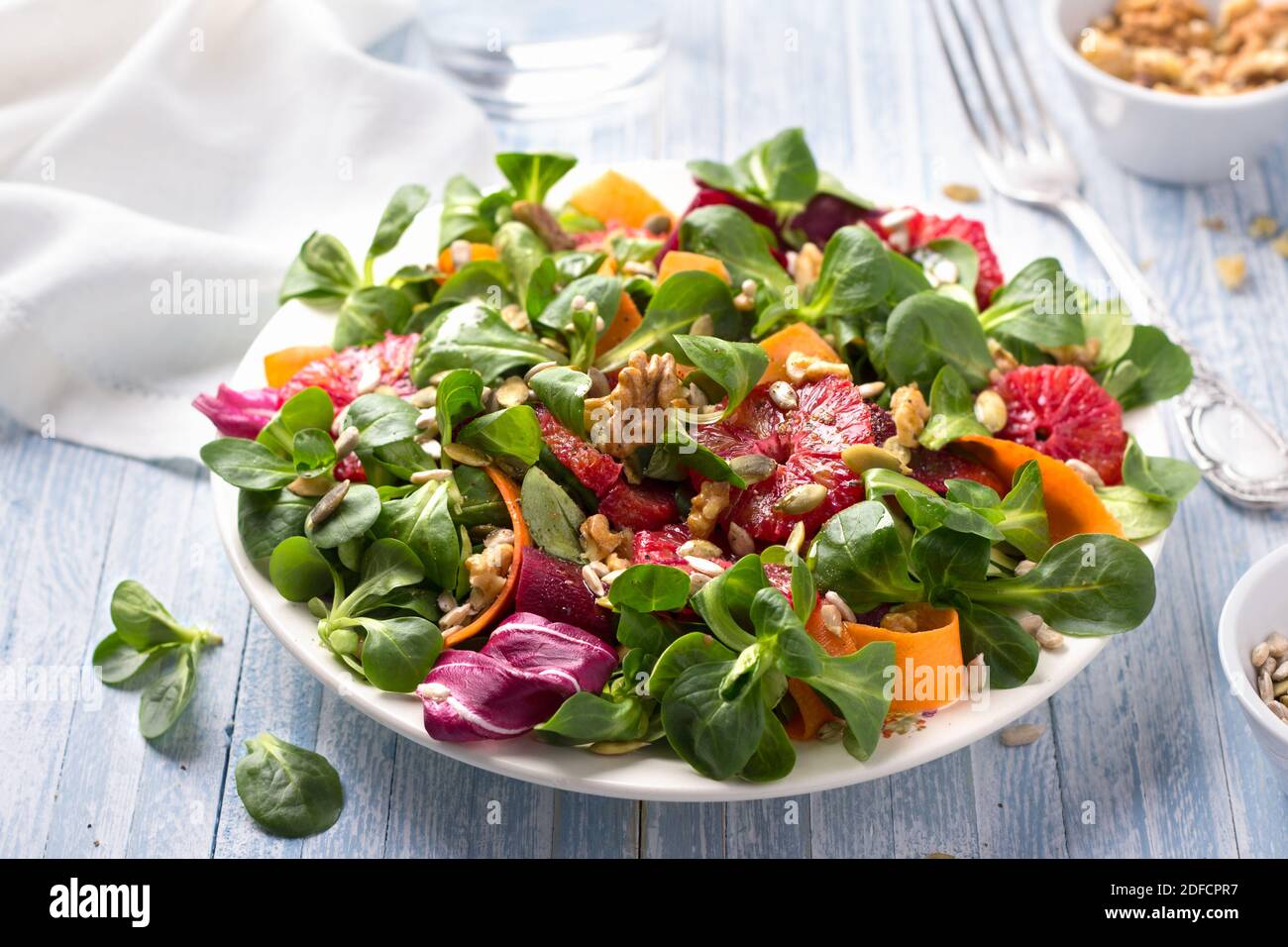Grüner Salat mit Blutorangen, Karotten, Rüben, Samen und Nüssen auf hellblauem Hintergrund, freier Platz. Leckere gesunde Lebensmittel Stockfoto