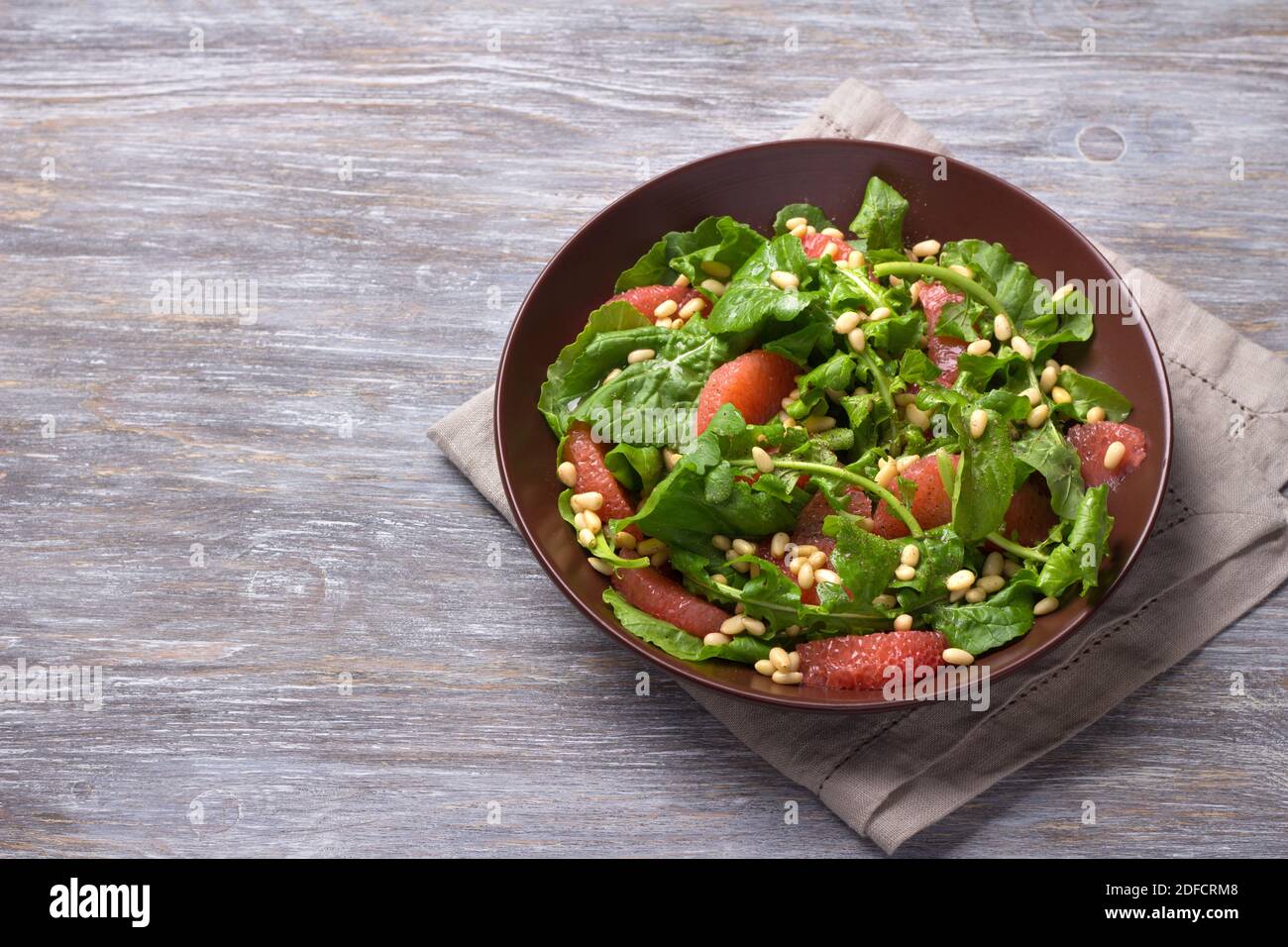 Frischer Salat aus Rucola mit Grapefruit und Pinienkernen auf Holzhintergrund. Gesundes, leckeres Essen Stockfoto