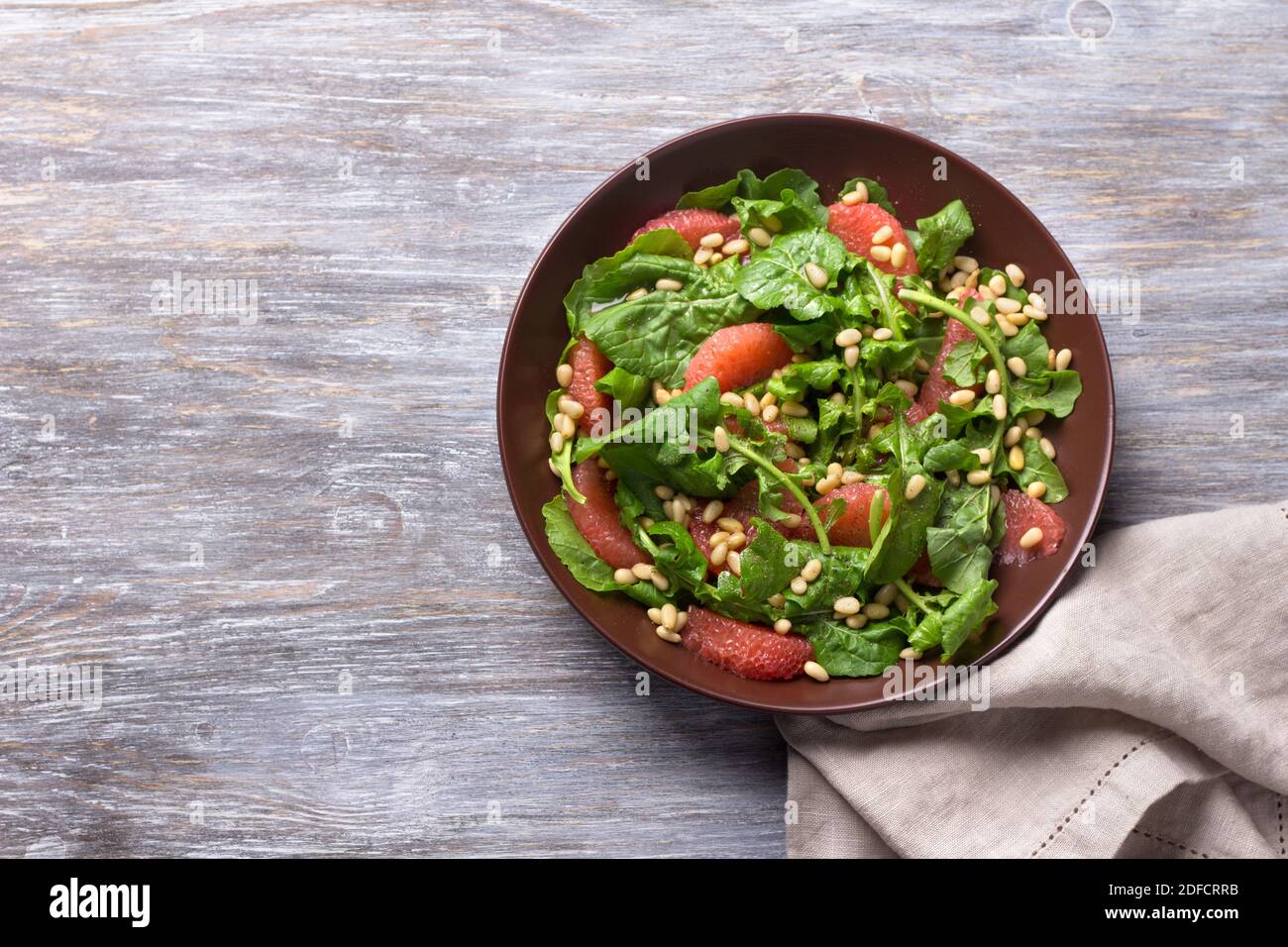 Frischer Salat aus Rucola mit Grapefruit und Pinienkernen auf Holzhintergrund. Gesundes, leckeres Essen Stockfoto