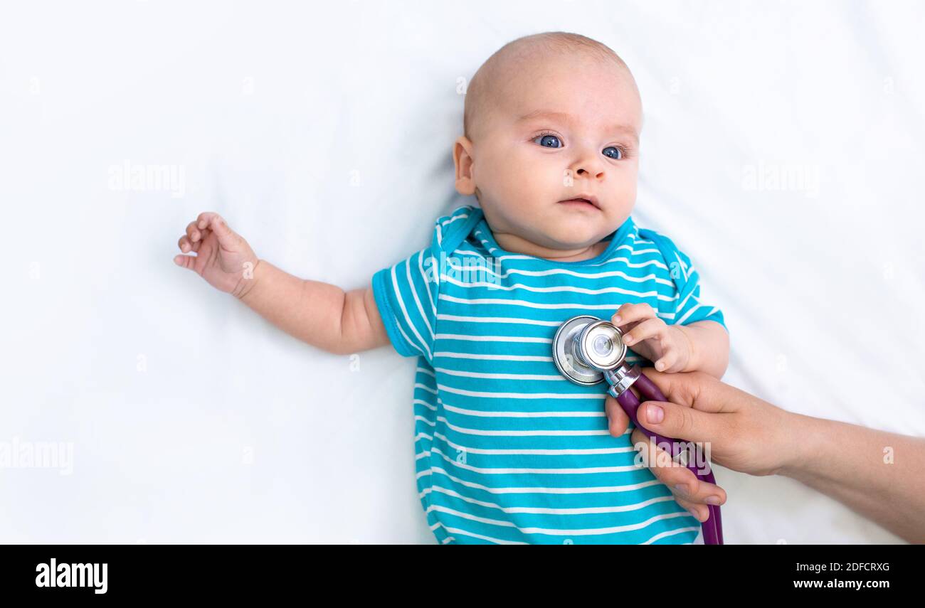 Medizinische Betreuung der Gesundheit eines Kindes. Das Neugeborene liegt auf einem weißen Bett, während es seine Lungen von einem Kinderarzt auskultiert Stockfoto