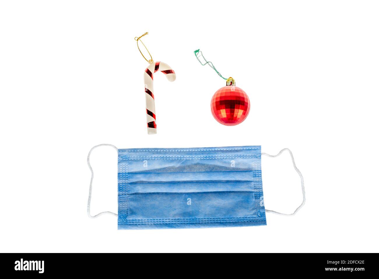 Weihnachtsdekoration auf weißem Hintergrund von Zuckerrohr, weihnachten rote Kugel und schützende medizinische Gesichtsmaske für Covid-19. Isoliert auf Weiß. Stockfoto