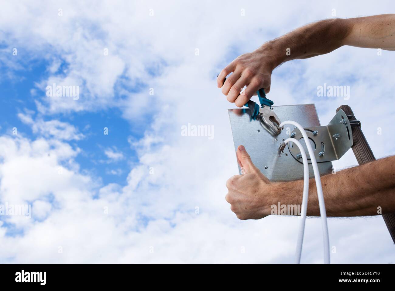 Man's Hände Installation 4G-Antenne auf bewölktem Himmel Hintergrund. Stockfoto